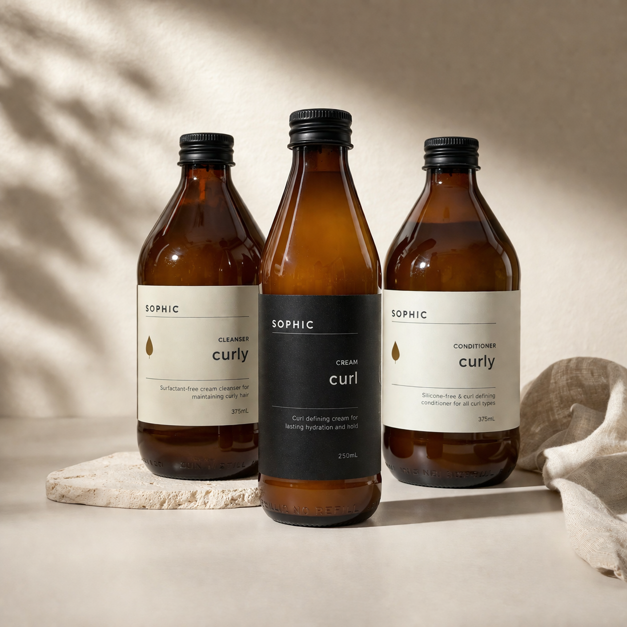 Three bottles of SOPHIC curly hair care products on a neutral background