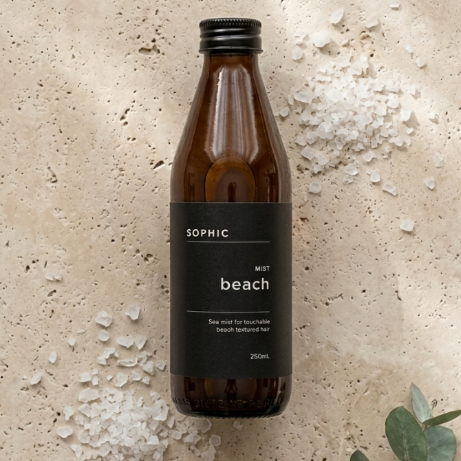 Brown bottle labeled 'SOPHIC' on a textured beige surface with eucalyptus leaves.