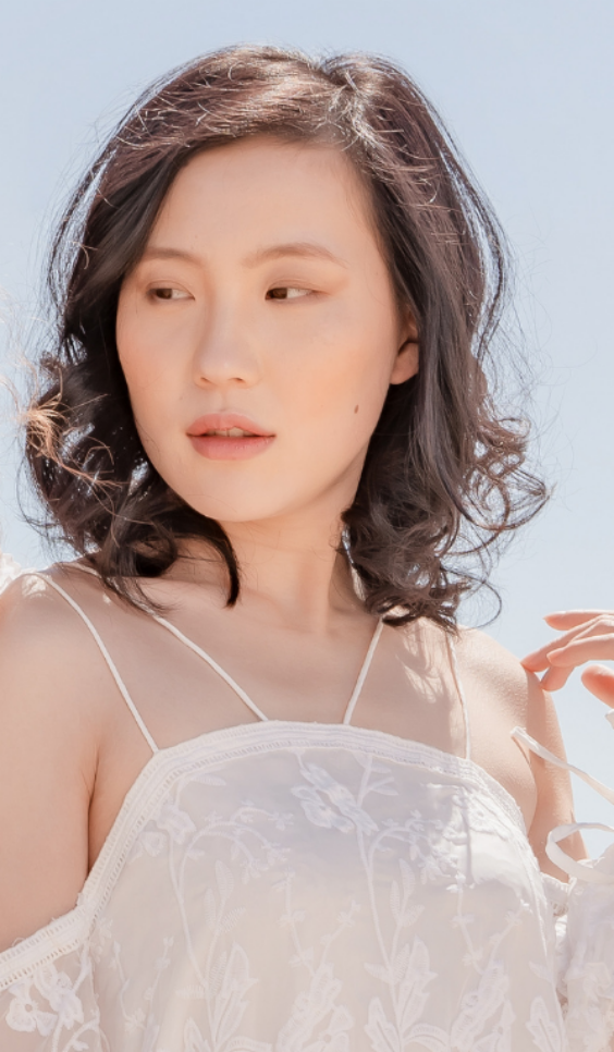 A promotional graphic featuring a woman in a white lace camisole centered over a coastal landscape background with green hills and blue ocean. Text reads 'MADE IN AUSTRALIA.
